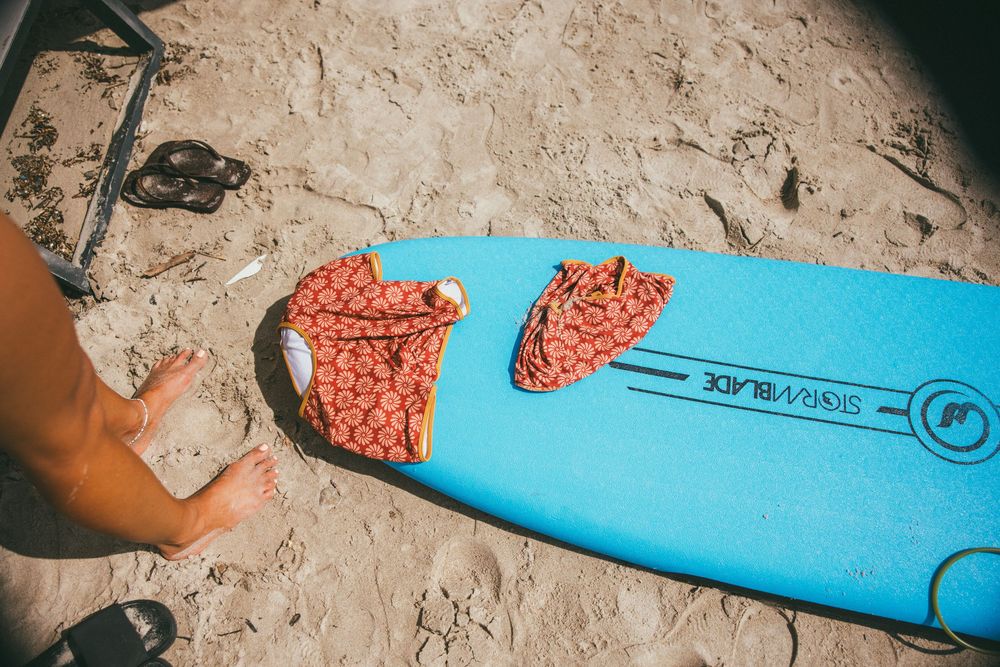 Close-up shots showing steps of surfboard repair process with blue and orange materials on sandy surface.