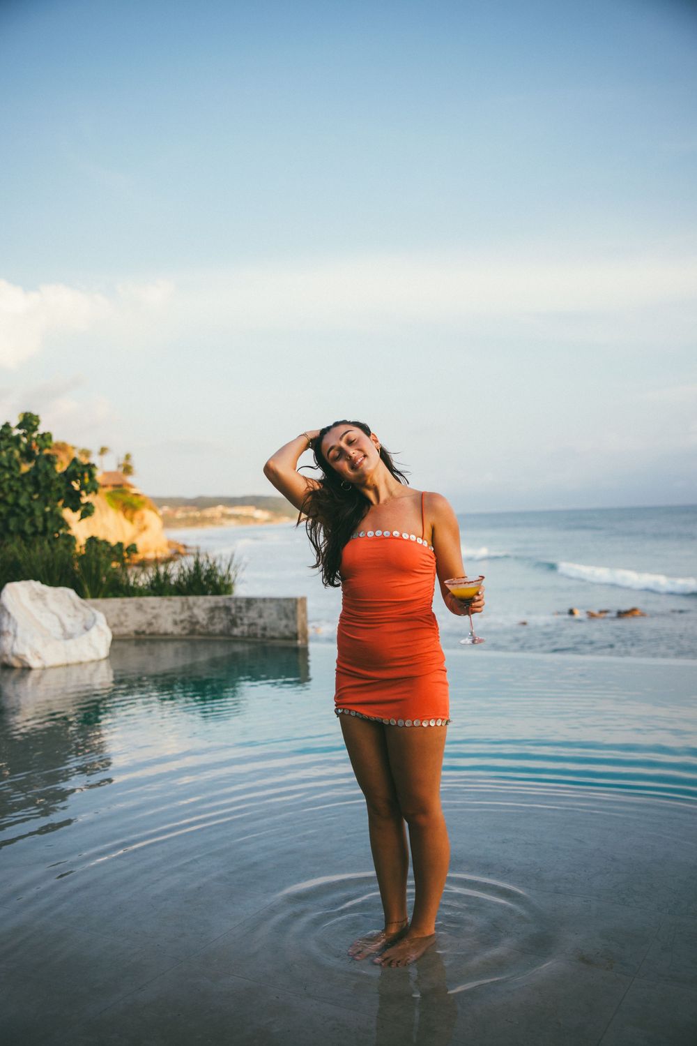 A series of photos showing someone in a red swimsuit enjoying an infinity pool overlooking the ocean at sunset.