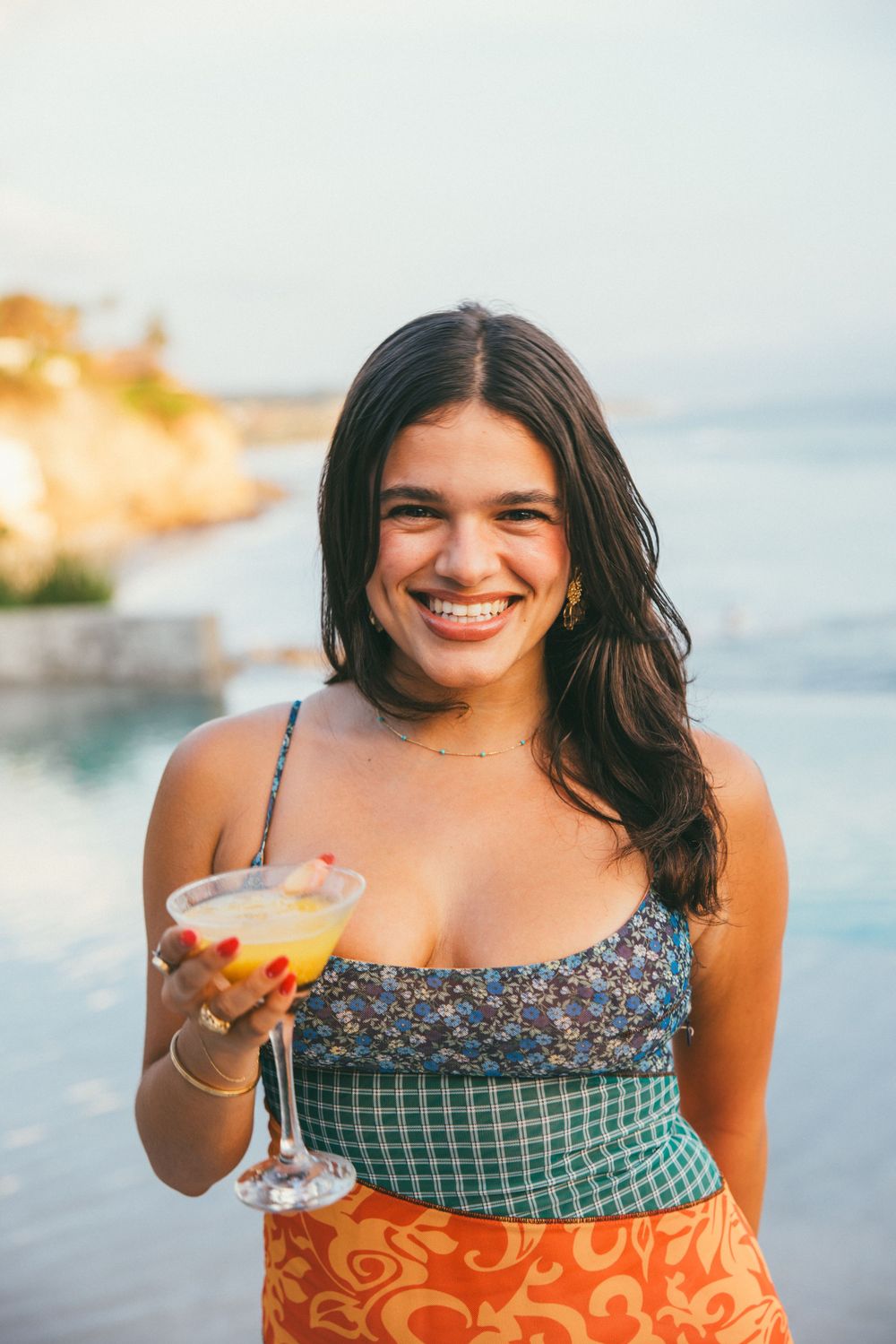 A series of beachside portraits showing someone wearing colorful summer dresses and holding cocktails.
