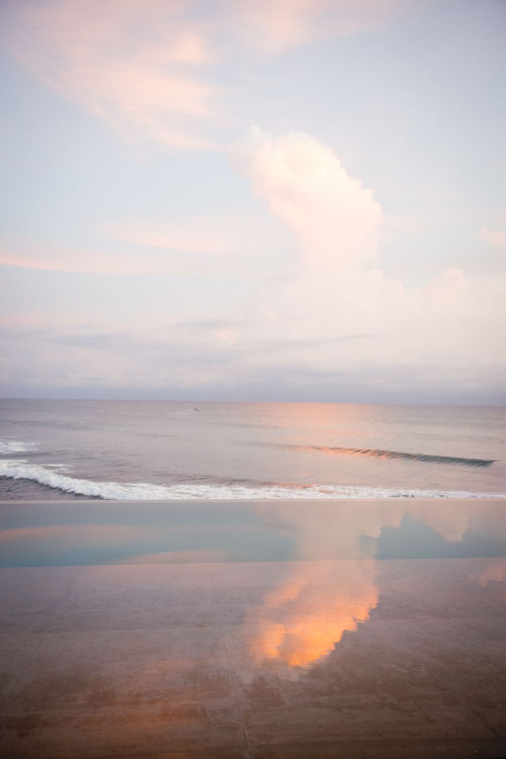 Panoramic view of a misty beach coastline at sunset with pink and orange clouds reflecting on the water.