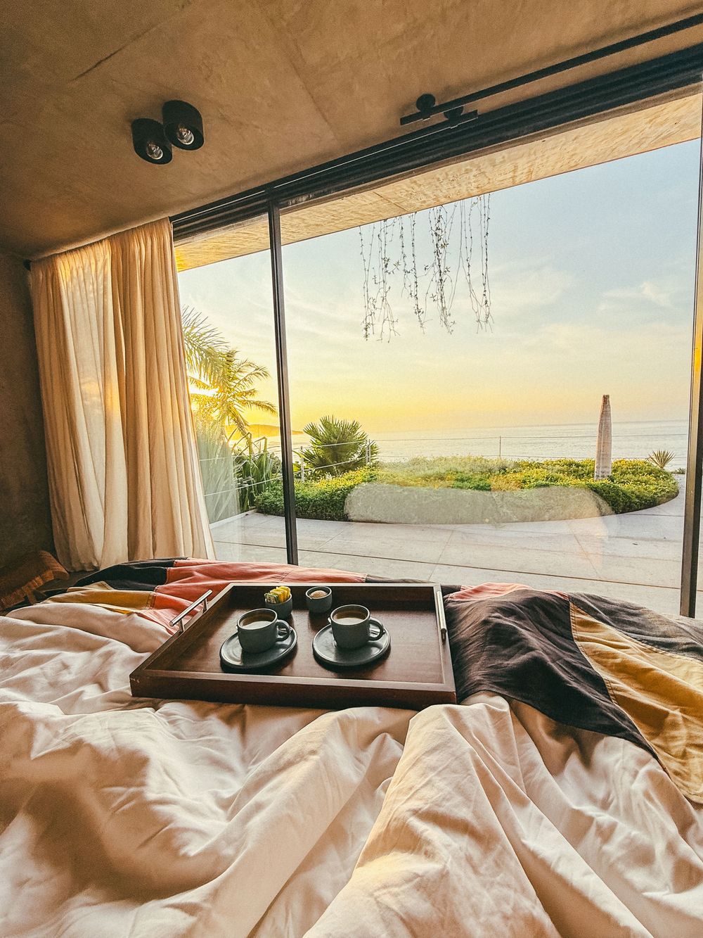 Luxurious oceanfront bedroom with white bedding and panoramic windows showcasing a stunning coastal sunrise view.