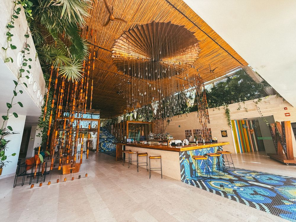Modern office hallway with wooden ceiling panels, blue and white striped floor, and hanging plants creating a natural ambiance.