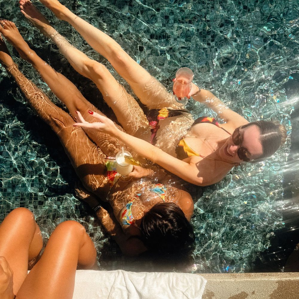 People relaxing in a luxurious pool with dark stone tiles and splashing water.