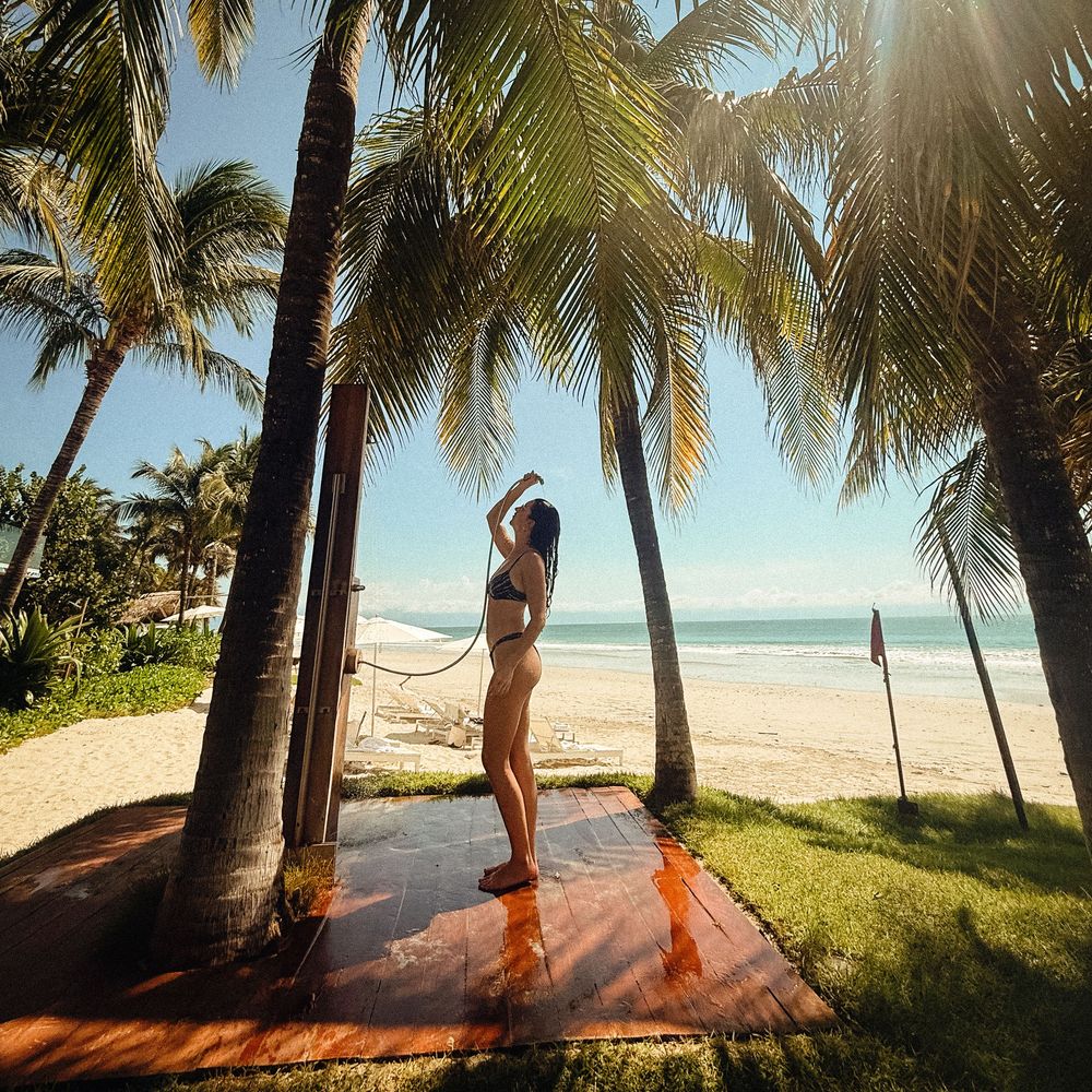 Palm trees line a wooden boardwalk along a pristine tropical beach under bright sunlight.