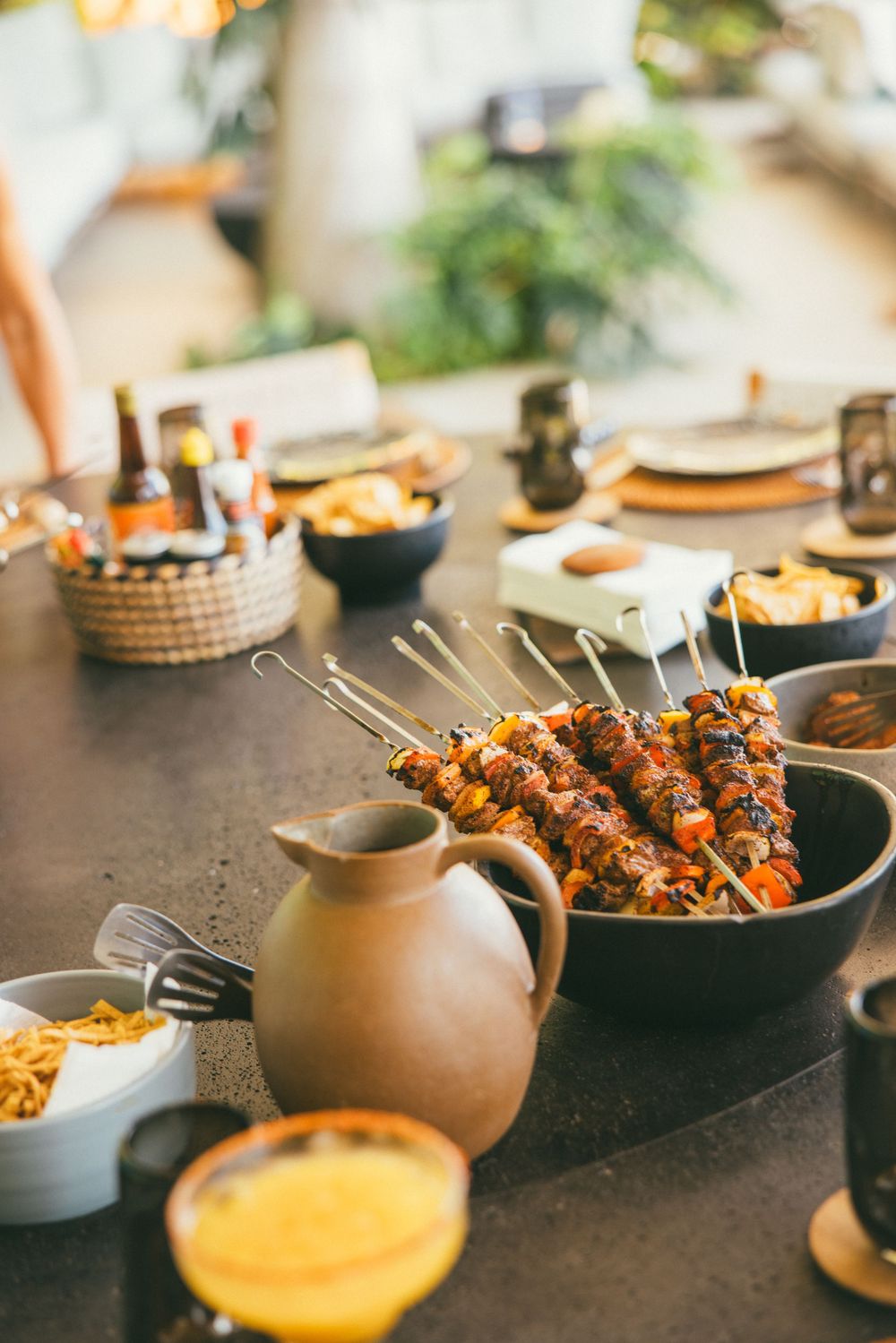 Rustic table spread with grilled skewers, sauces, and appetizers in earthenware bowls.