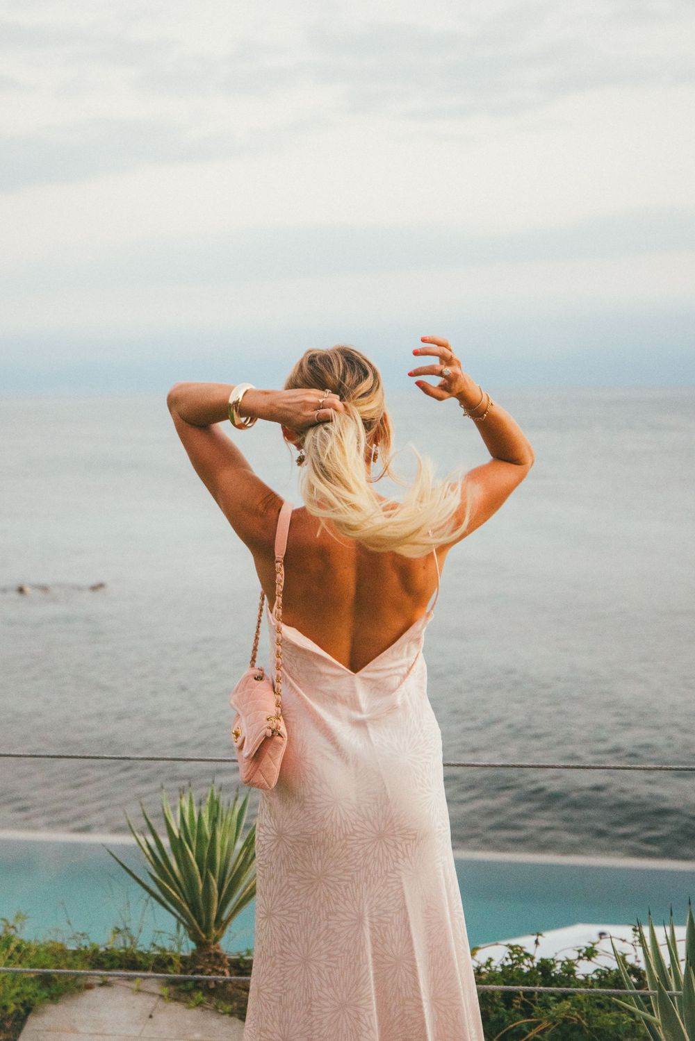 Person in a pink dress enjoying the ocean view from a coastal viewpoint with agave plants in the foreground.