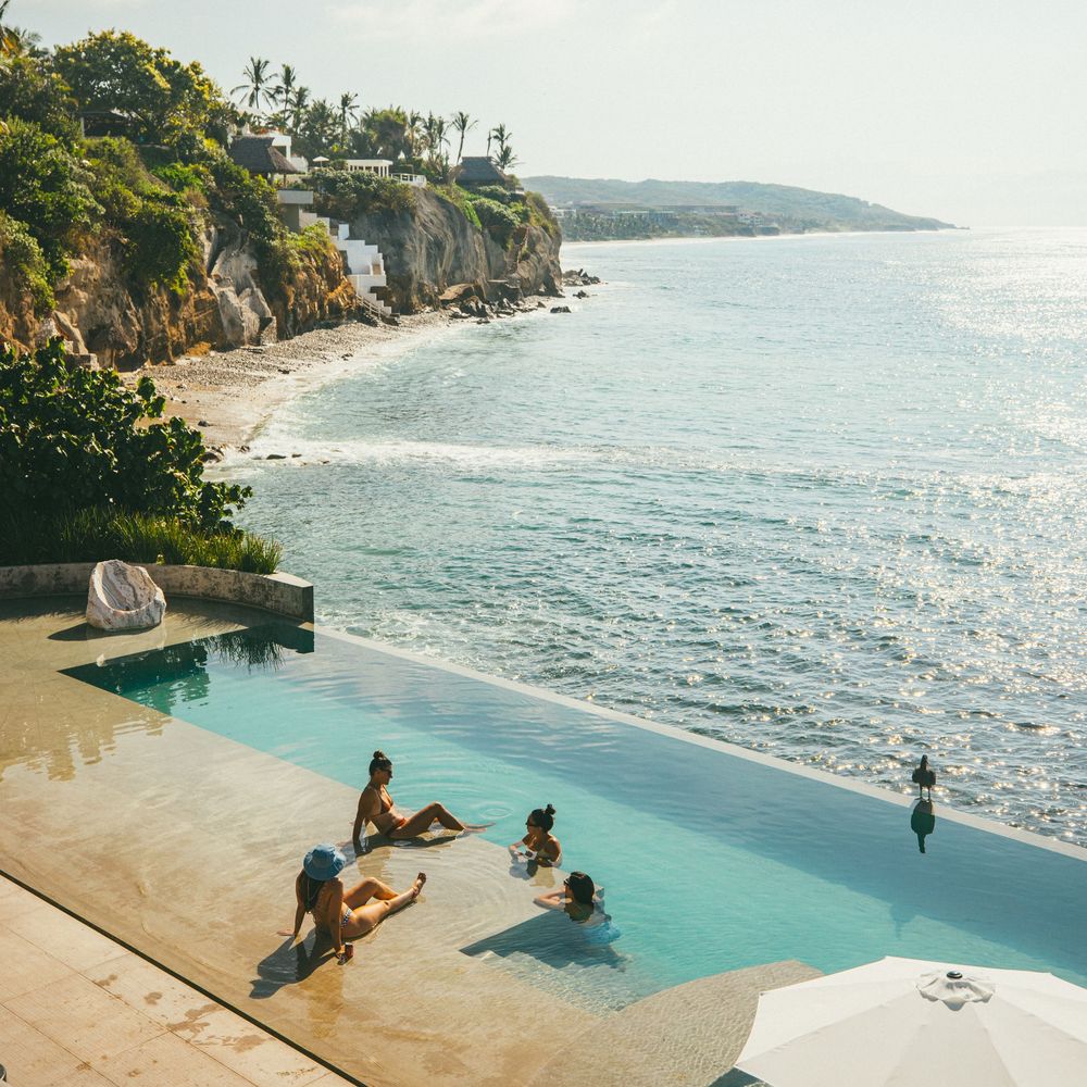 Luxury infinity pool overlooking dramatic ocean cliffs with people lounging poolside.