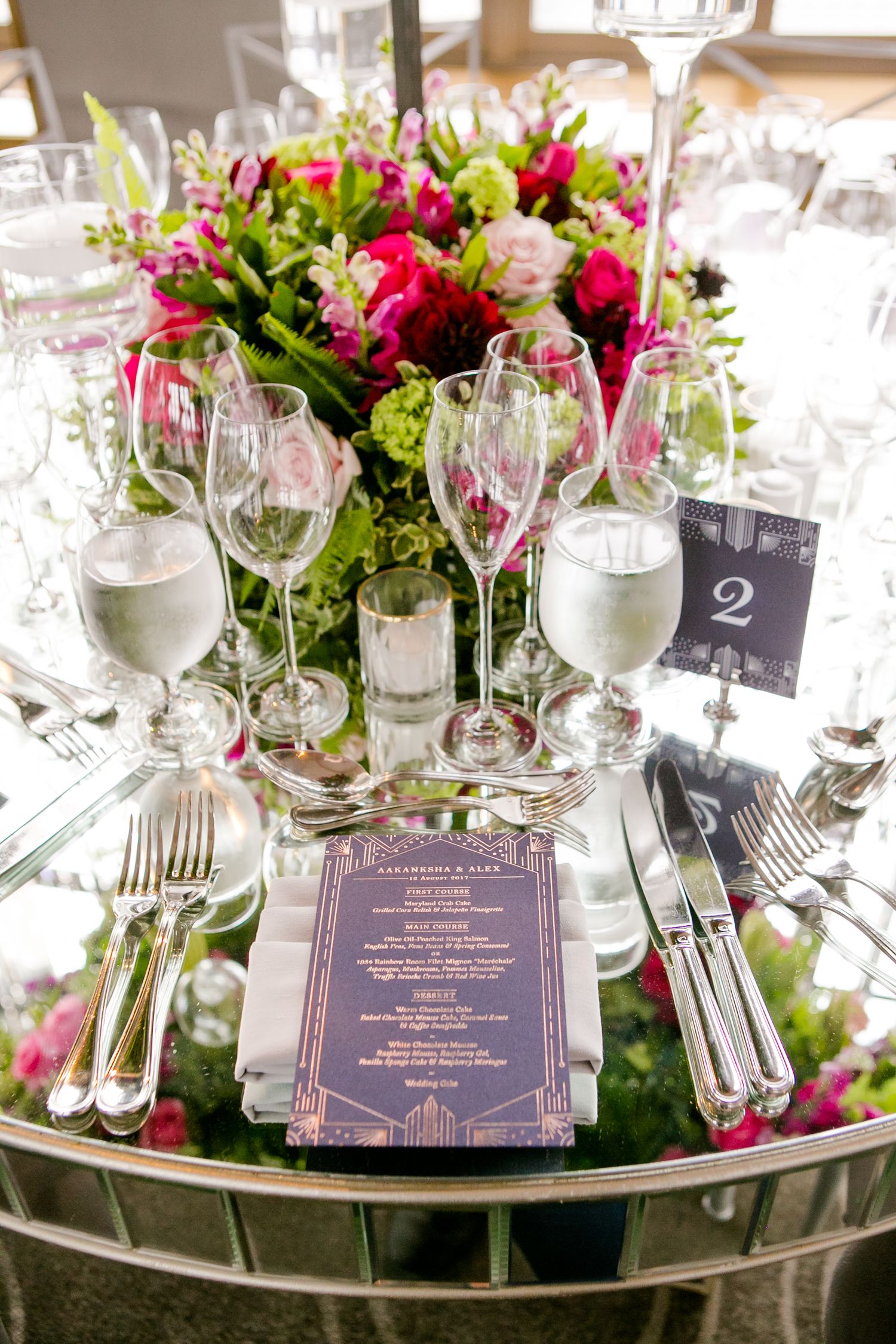 Elegant table settings with pink floral centerpieces and navy blue menus at a wedding reception.