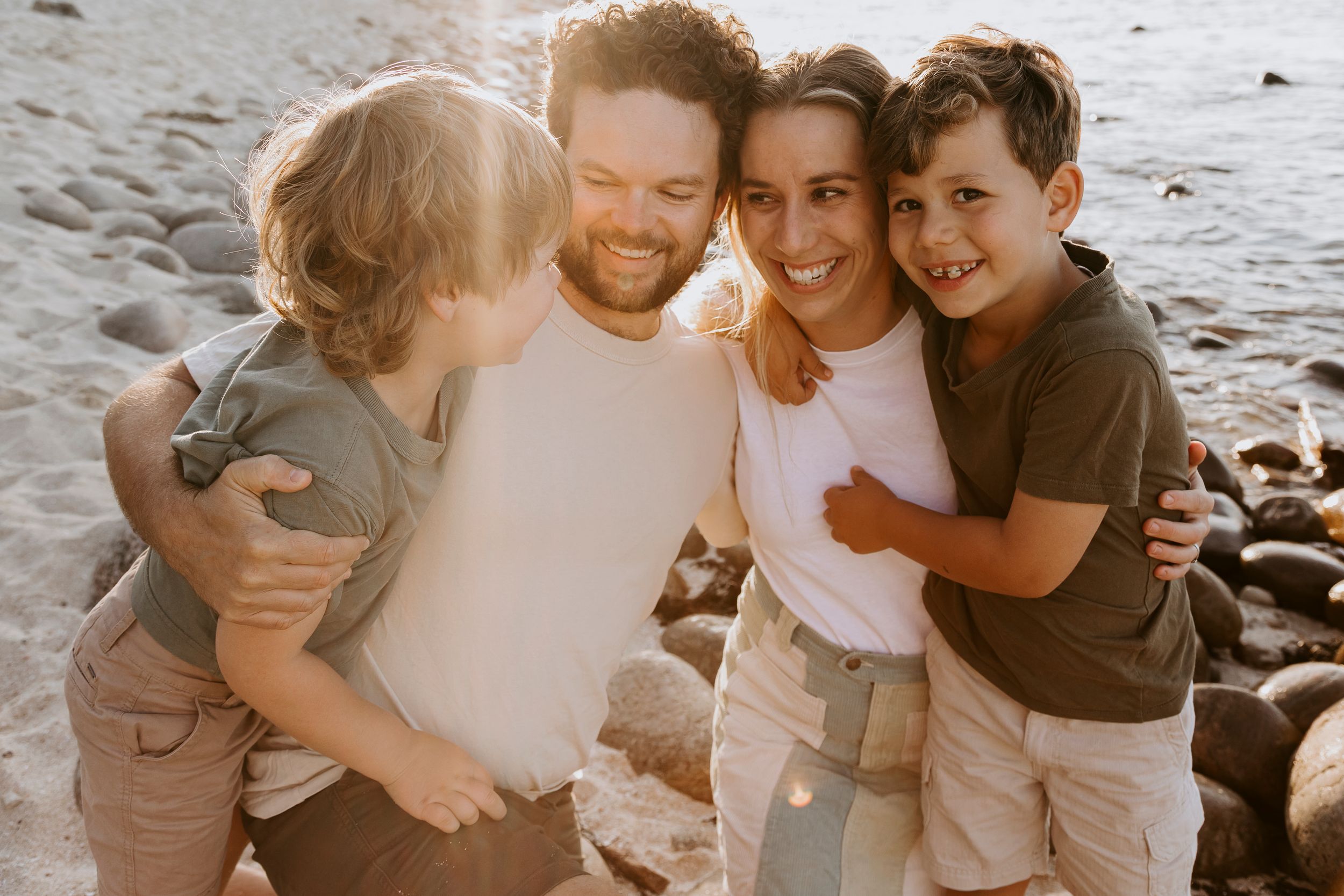 Happy family sharing a joyful moment together on a rocky beach during golden hour.
