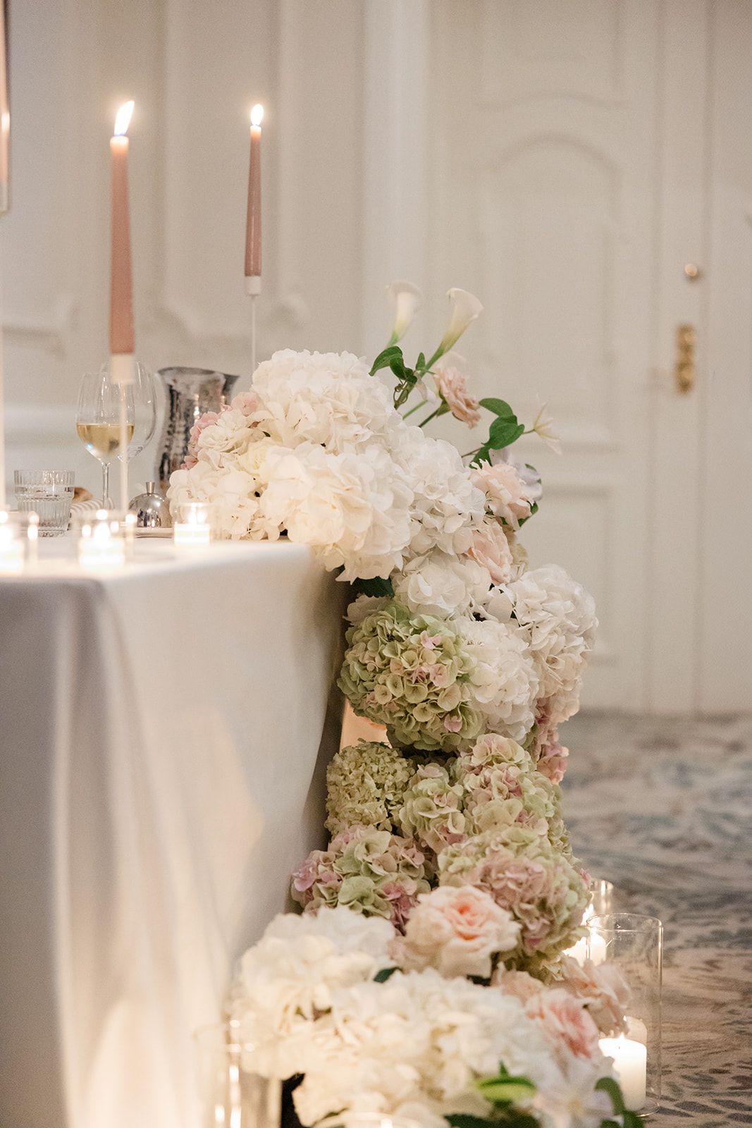Elegant wedding table setting with blush pink roses, striped napkins, and white plates on a crisp white tablecloth.