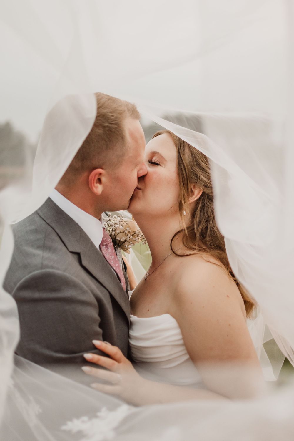 A romantic wedding couple shares tender kisses under a flowing white veil in a series of intimate portraits.