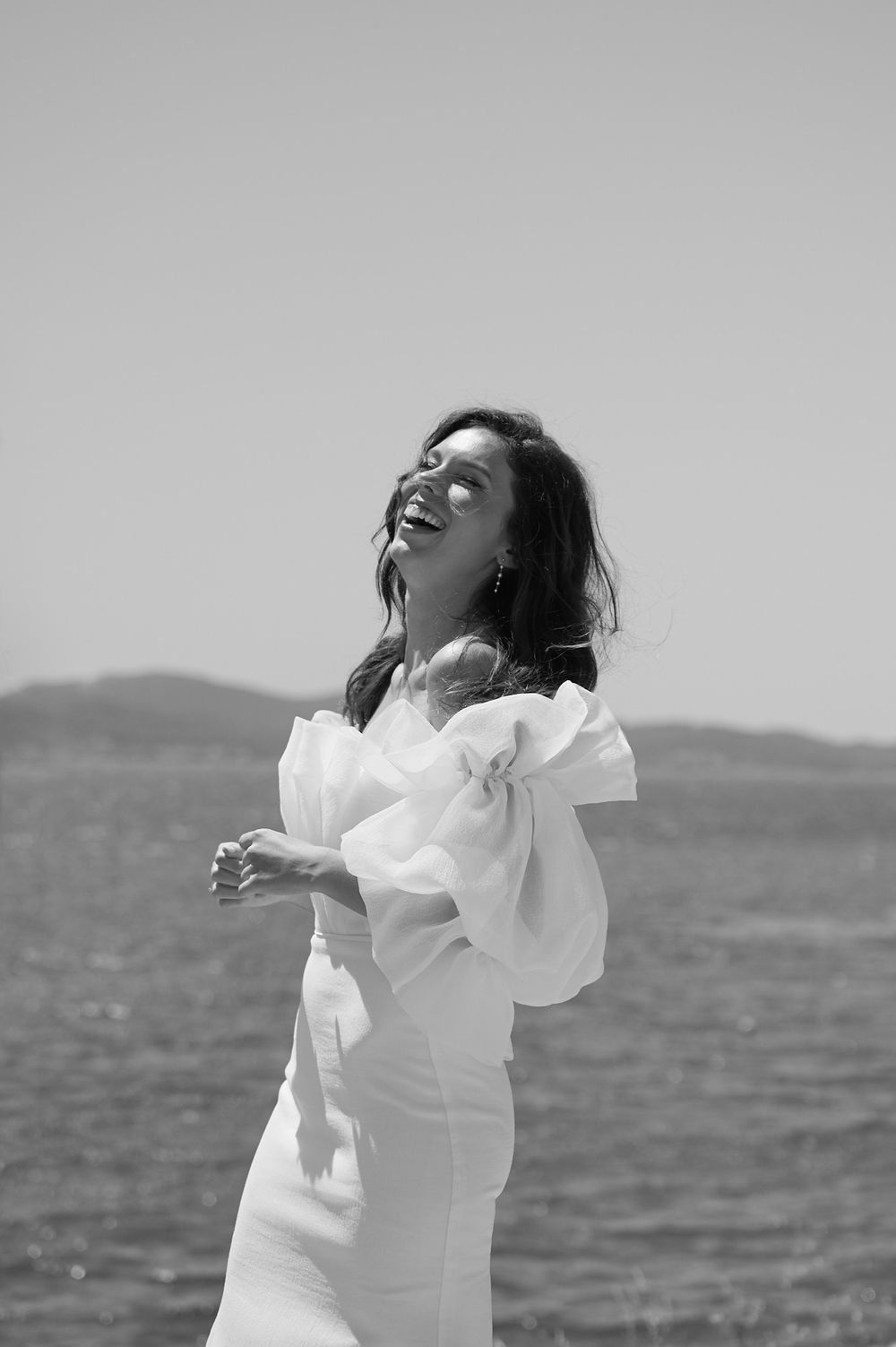 Black and white portrait of a bride in a white dress against a seaside backdrop.