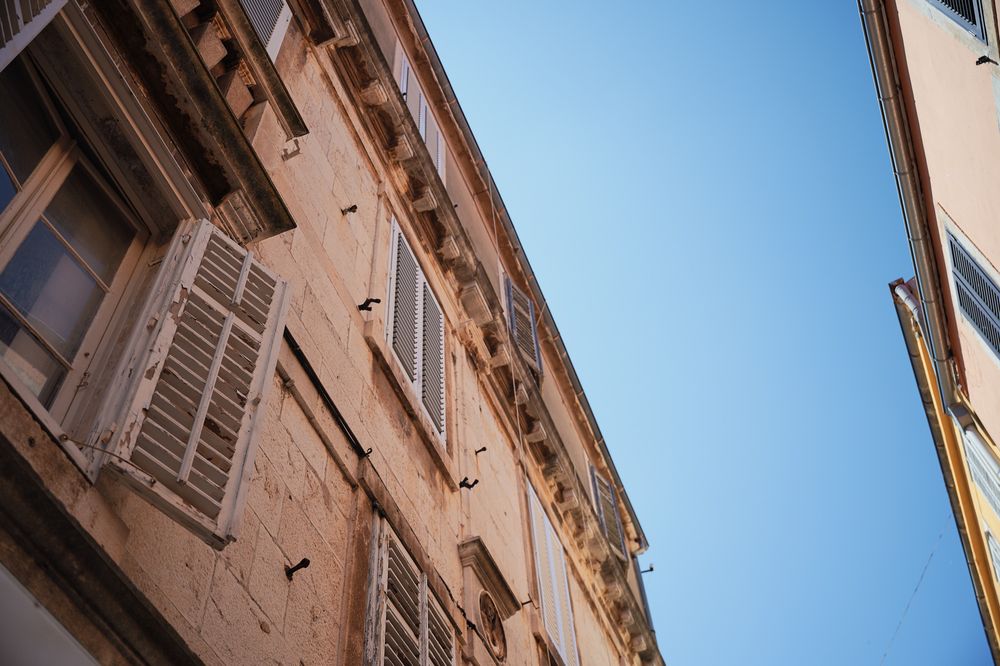 Looking up at traditional Mediterranean architecture with blue sky and shuttered windows.