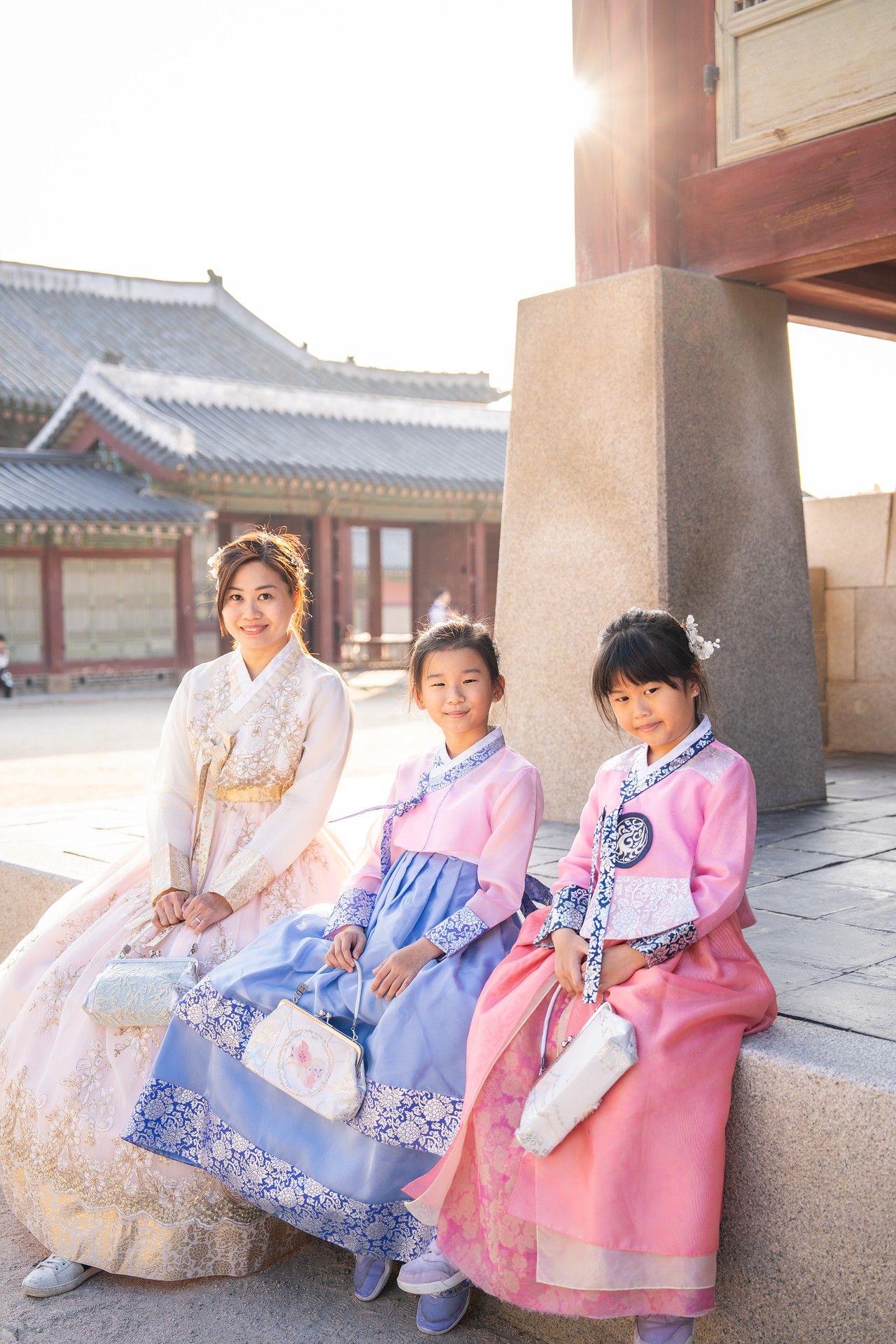Children in colorful traditional Korean hanbok clothing sit together along a temple corridor.
