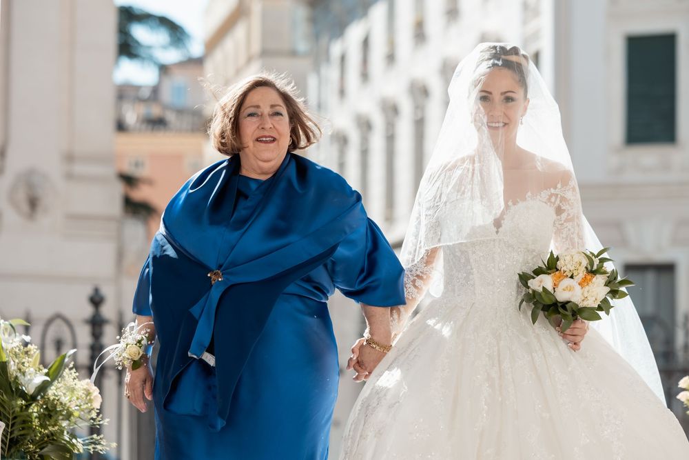 A joyful wedding party walks down a bright city street in blue and white attire.