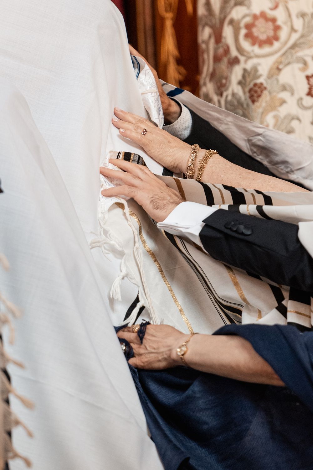 Multiple hands reach out to adjust a white wedding dress during a traditional Jewish ceremony preparation.