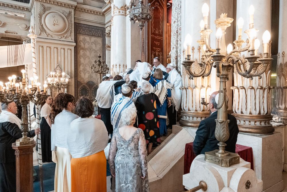 Elegant wedding party gathers in ornate white and gold ballroom with crystal chandeliers and classical architecture.