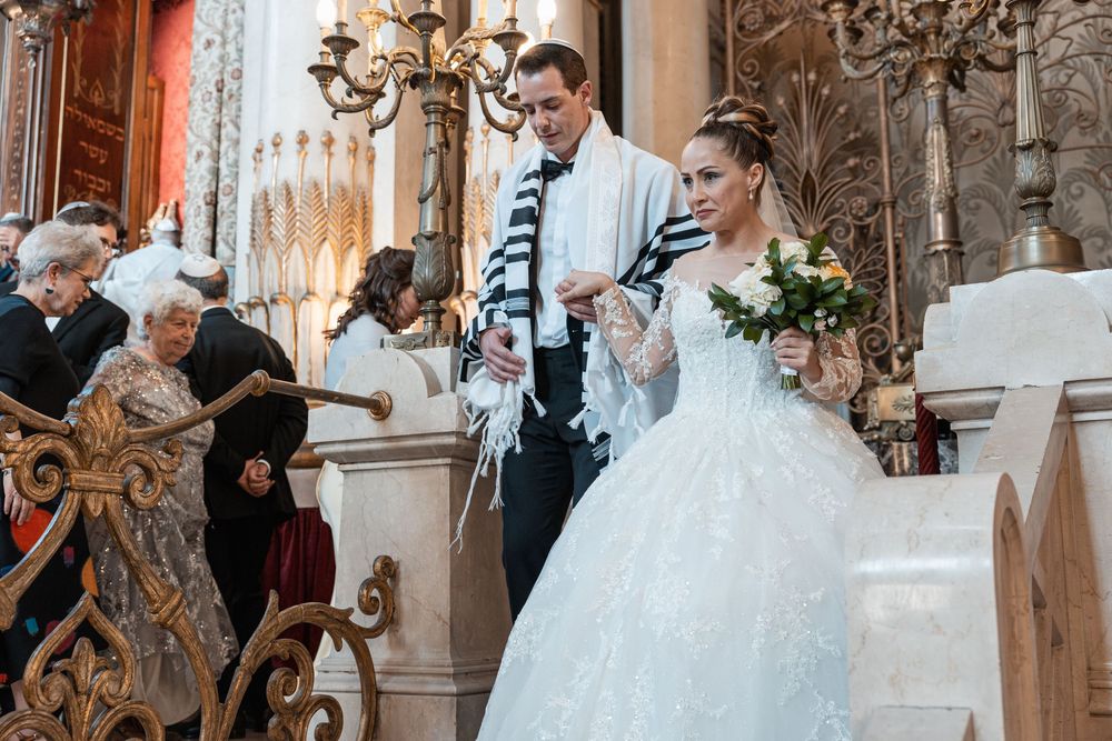 A wedding celebration in an ornate church venue with guests gathered around the happy couple during the ceremony.