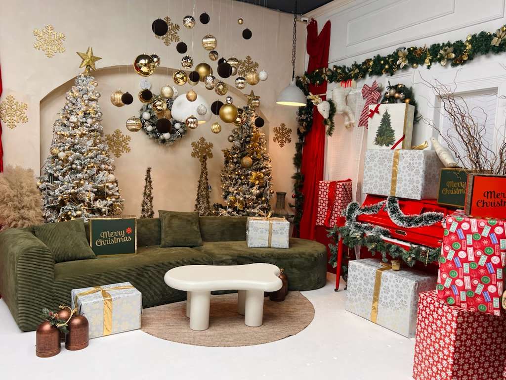 Christmas studio set with green sofa, gold and white decorated trees, wrapped gifts, and festive ornaments.