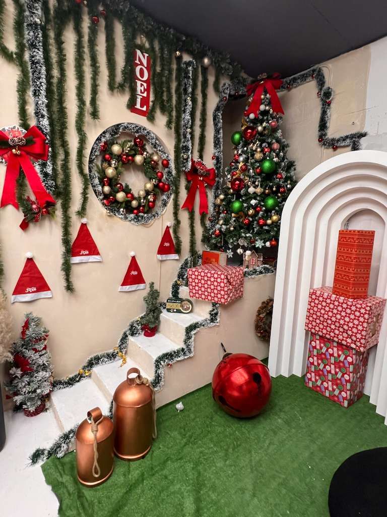 Colorful Christmas photo set featuring NOEL sign, wreaths, Santa hats, decorated tree, and large ornaments.