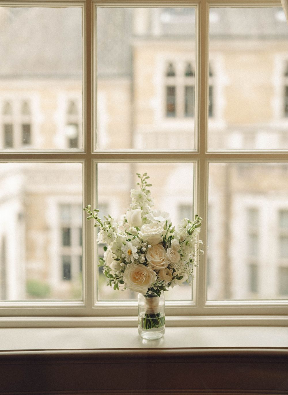 White roses and floral arrangements displayed along bright windowsill in elegant room.