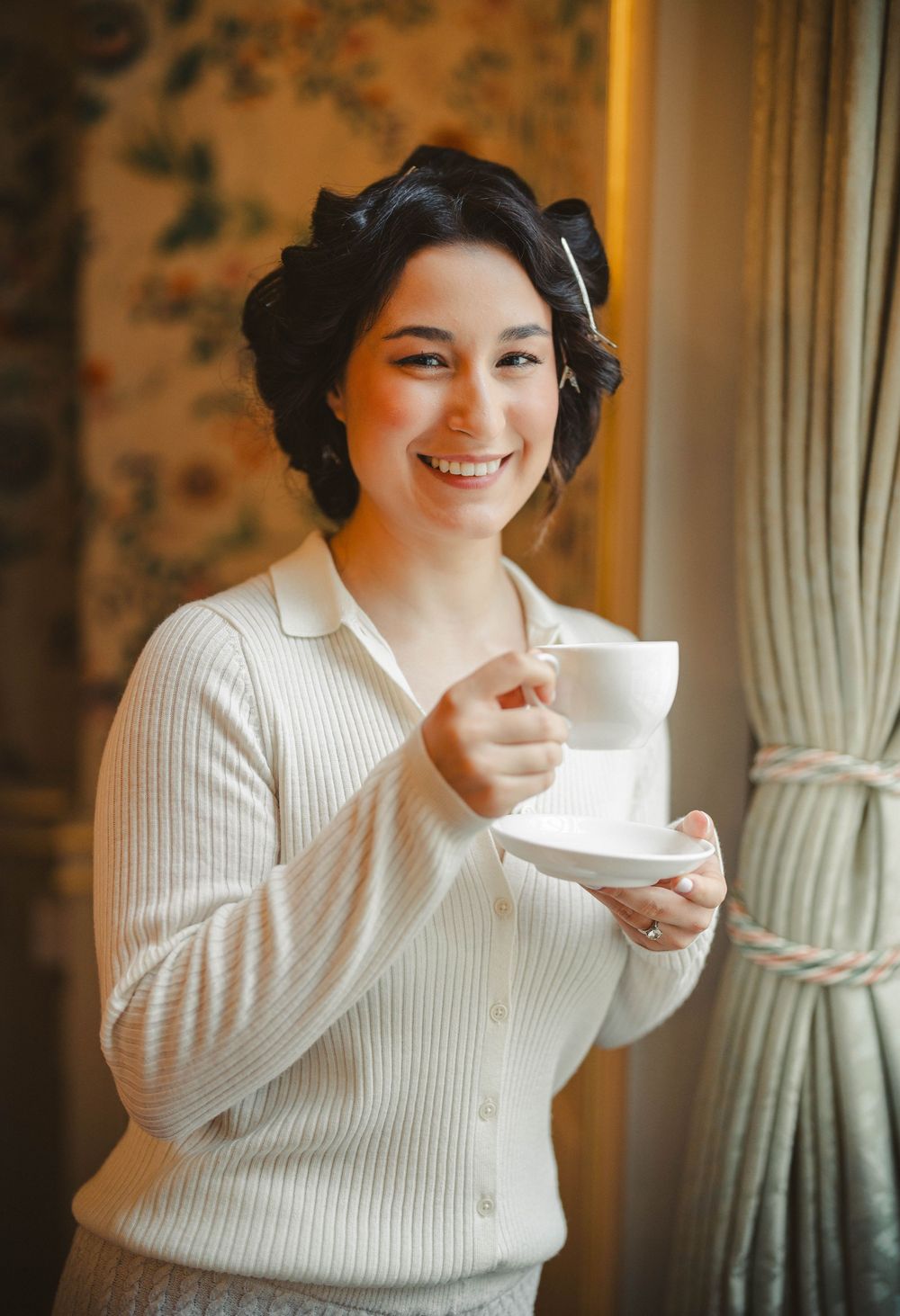 Person in white sweater enjoying tea from a delicate teacup.