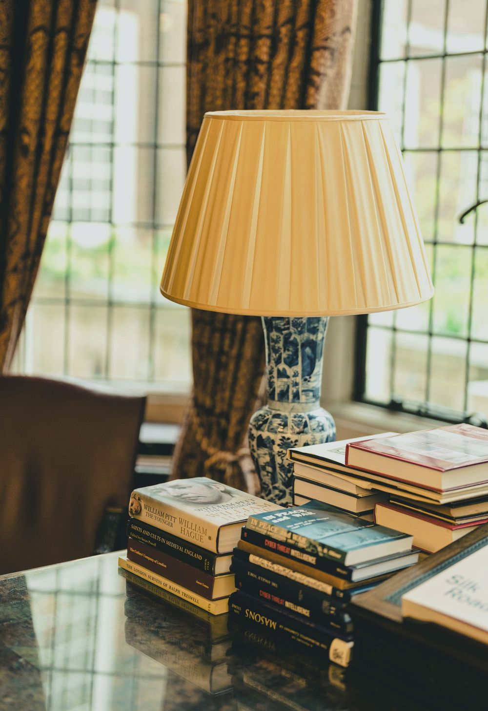 Table lamp with pleated shade next to stacked books in an elegant interior setting.