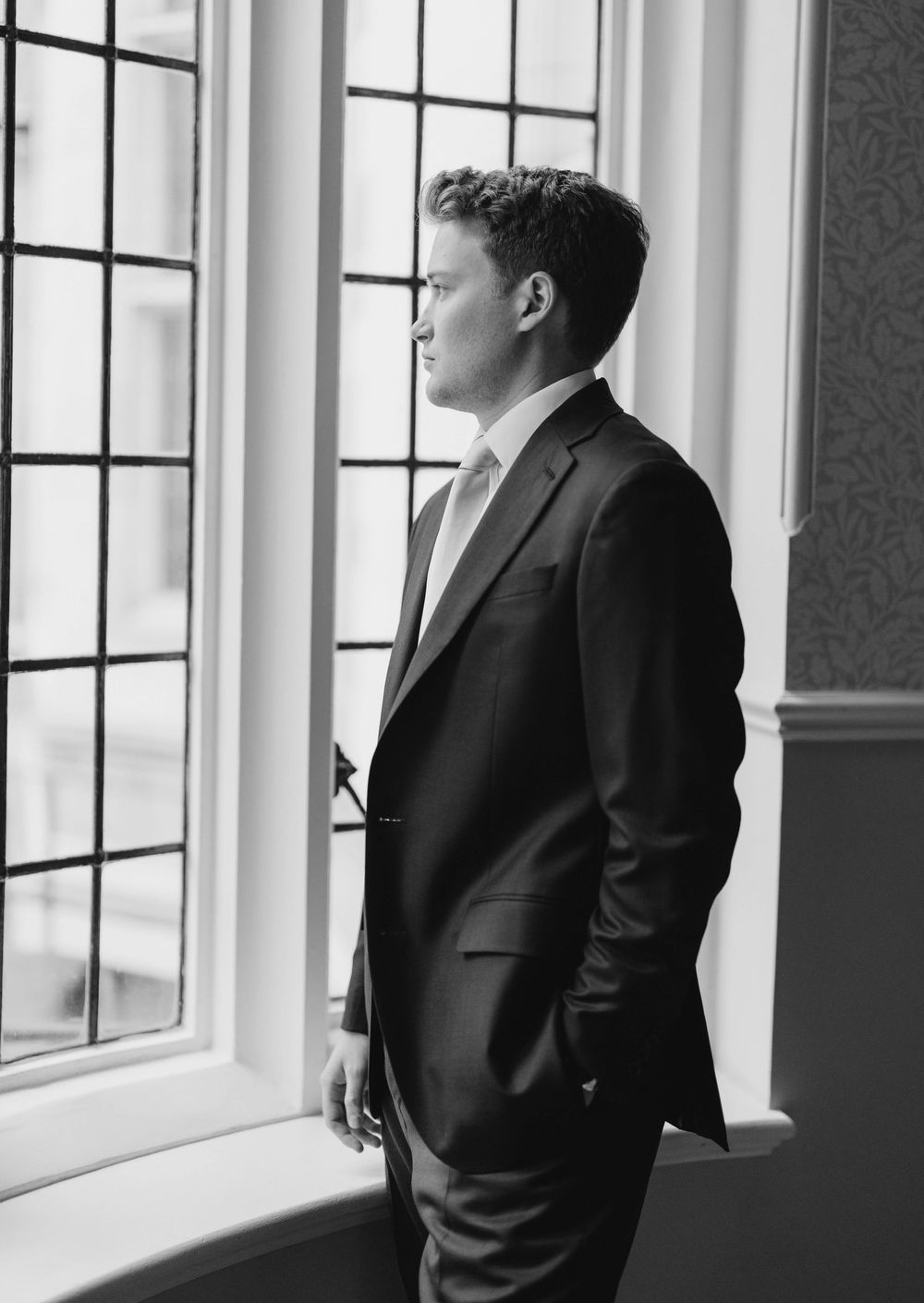Silhouetted figures stand contemplatively by large windows in formal attire.