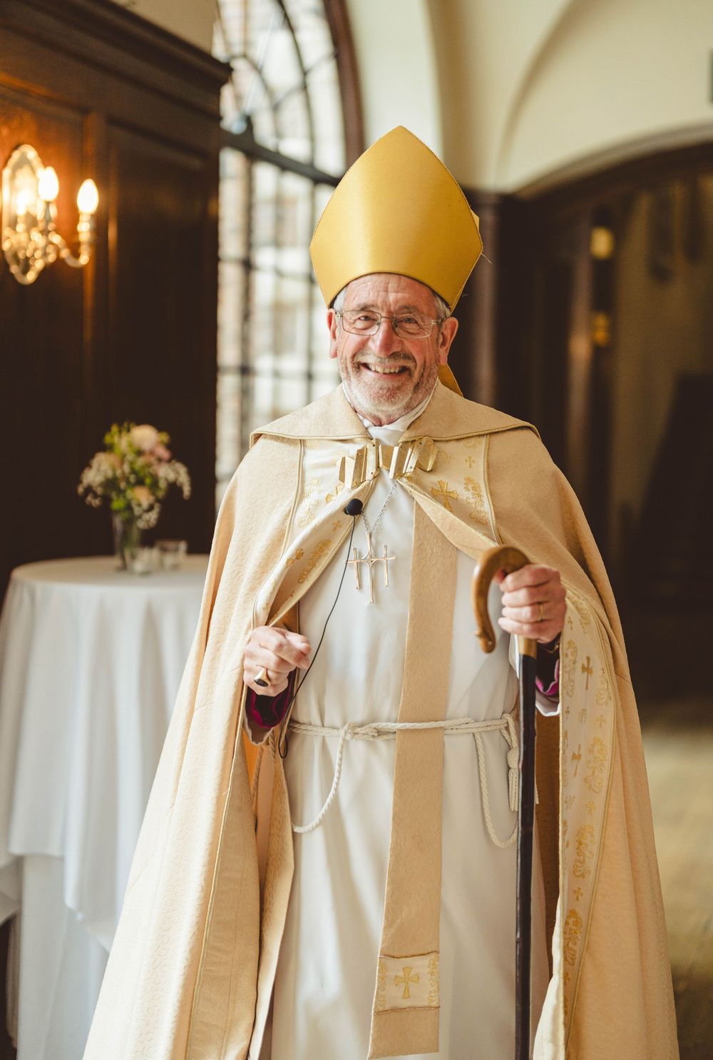 Religious officiant in cream colored ceremonial robes smiling during wedding ceremony.