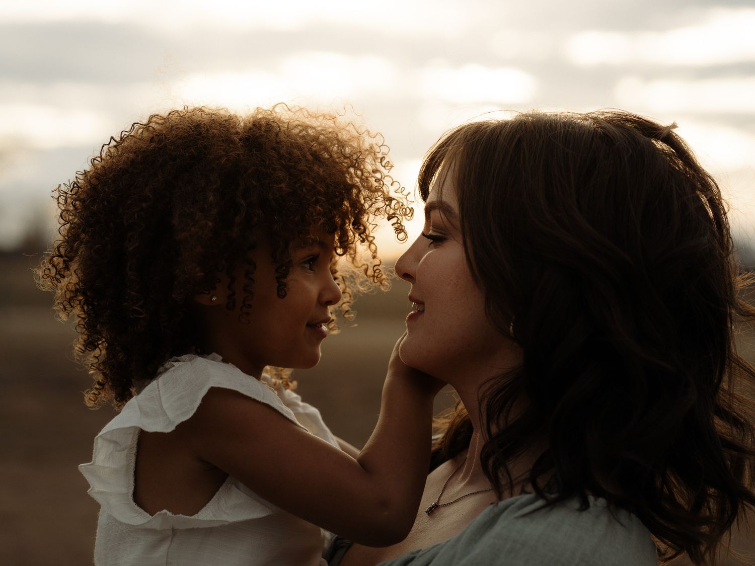 A tender moment at sunset shows a parent lifting a child in a white dress while spinning in a golden field.