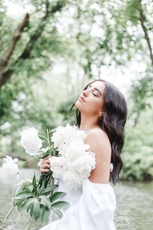 A romantic outdoor photoshoot with white peonies and a flowing dress against a lush green garden backdrop.
