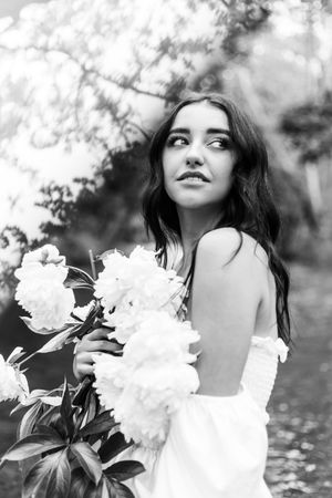 Ethereal black and white portrait with white flowers and an off-shoulder dress in a garden setting.