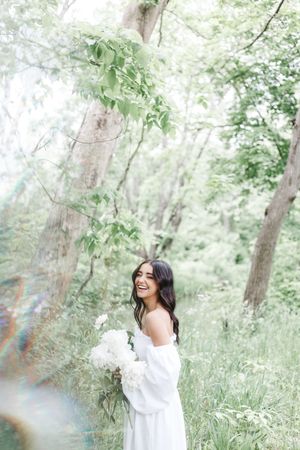 A dreamy outdoor photoshoot in a lush forest setting with soft natural lighting and white floral accents.