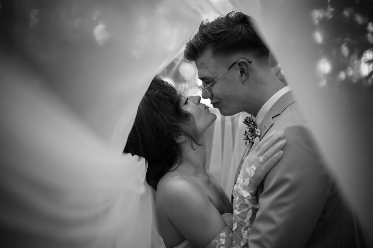 Black and white romantic portrait of bride and groom nearly kissing with soft bokeh background lighting.