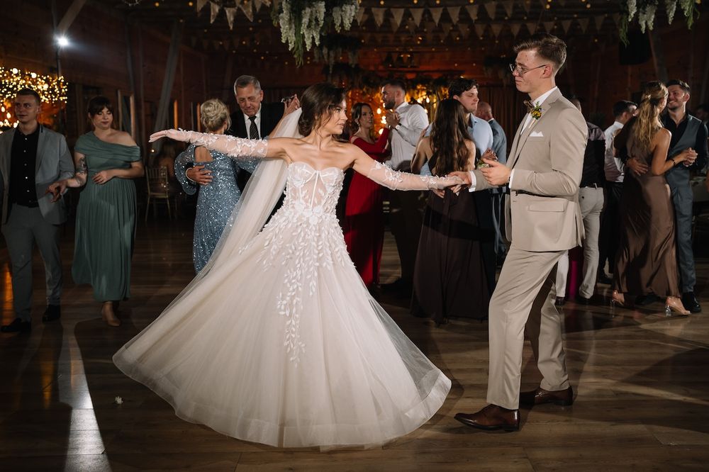 Bride in a floral lace gown twirls elegantly with groom in beige suit during wedding reception dance.