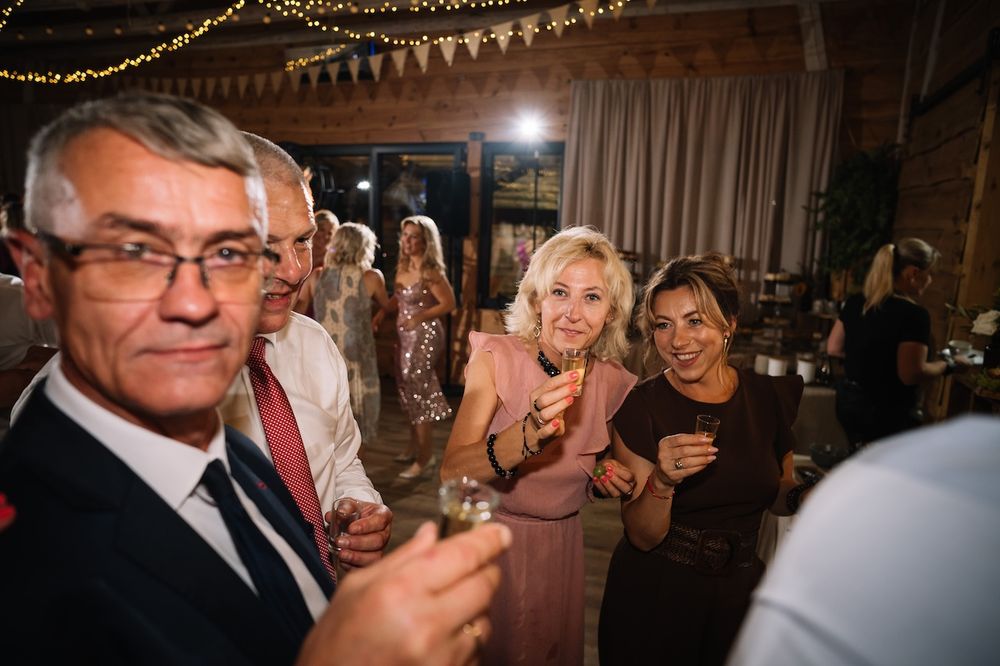 Smiling wedding guests raise glasses in a toast during a warm and festive evening reception celebration.