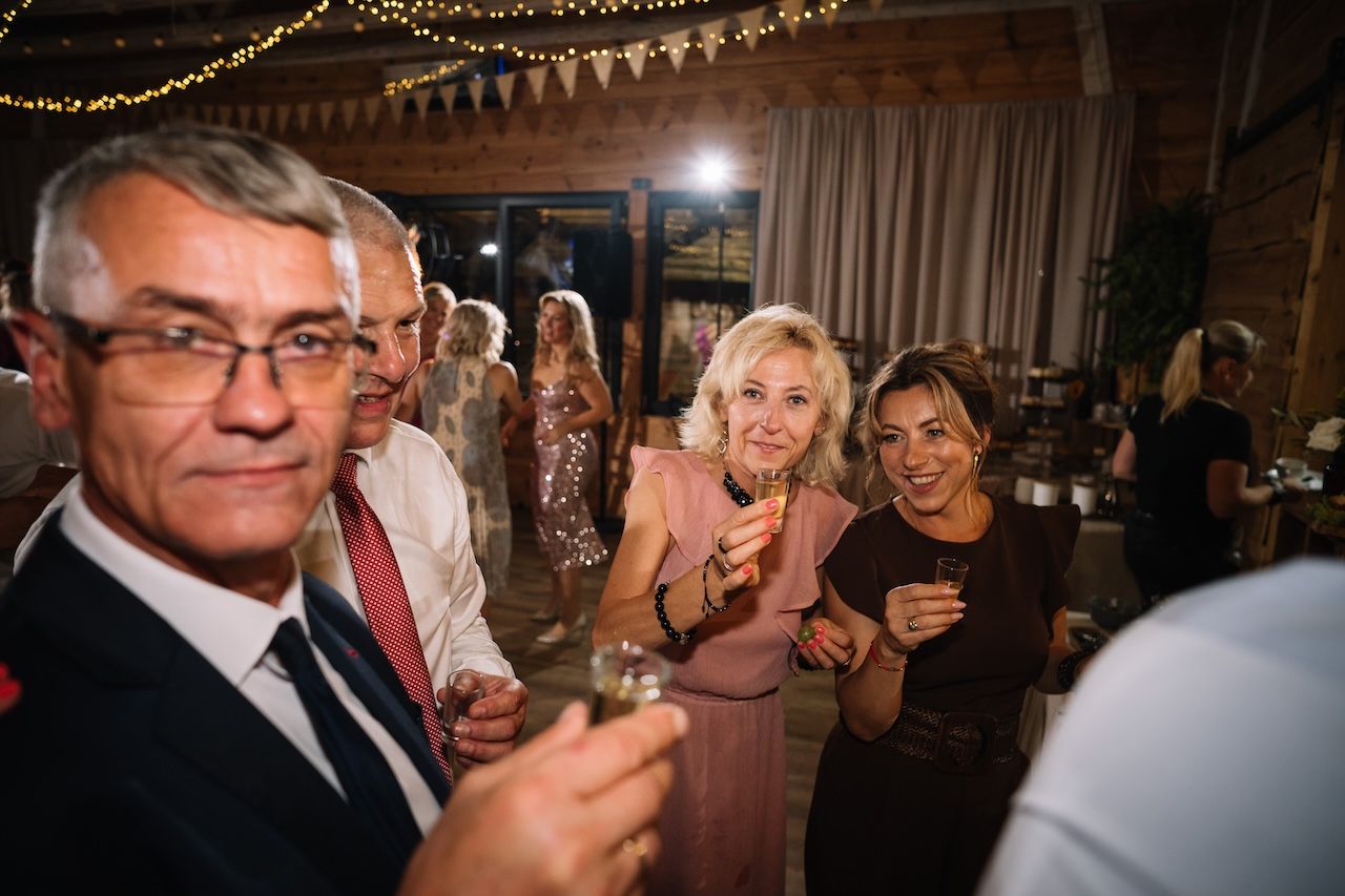 Smiling wedding guests raise glasses in a toast during a warm and festive evening reception celebration.