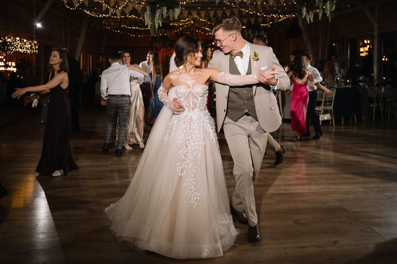Bride and groom share romantic first dance in elegant barn wedding venue with warm string lights.