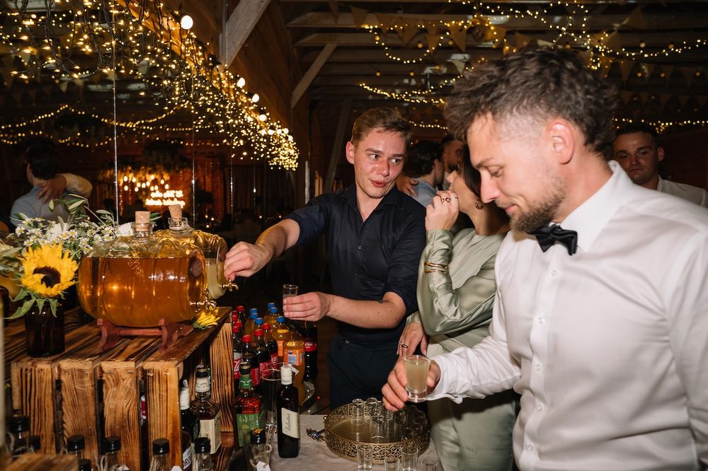 Bartender serves drinks at rustic wooden bar decorated with sunflowers and string lights.
