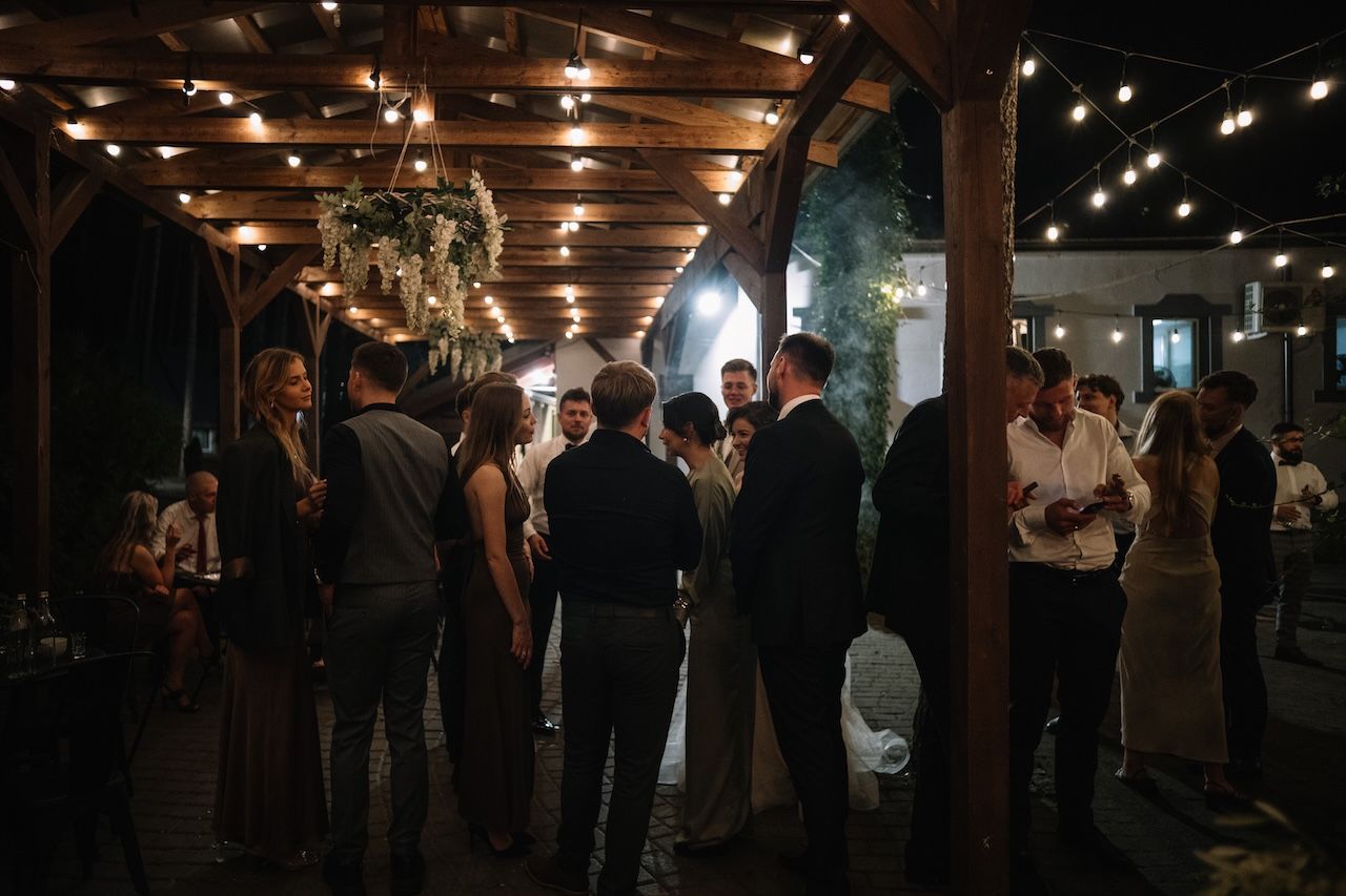 Wedding guests socialize outdoors under warm string lights during evening reception.
