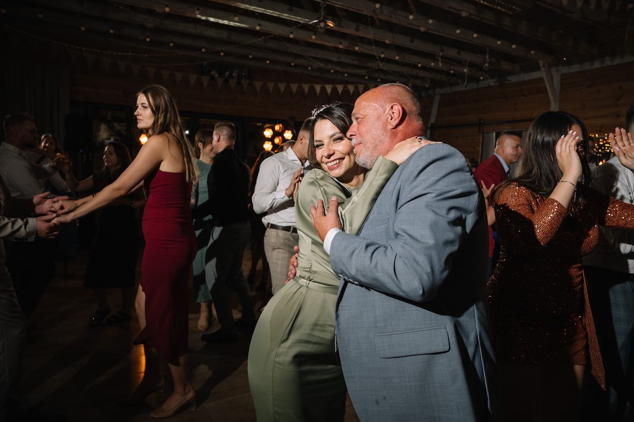 Guests dancing and embracing joyfully at a rustic wedding reception with warm ambient lighting.