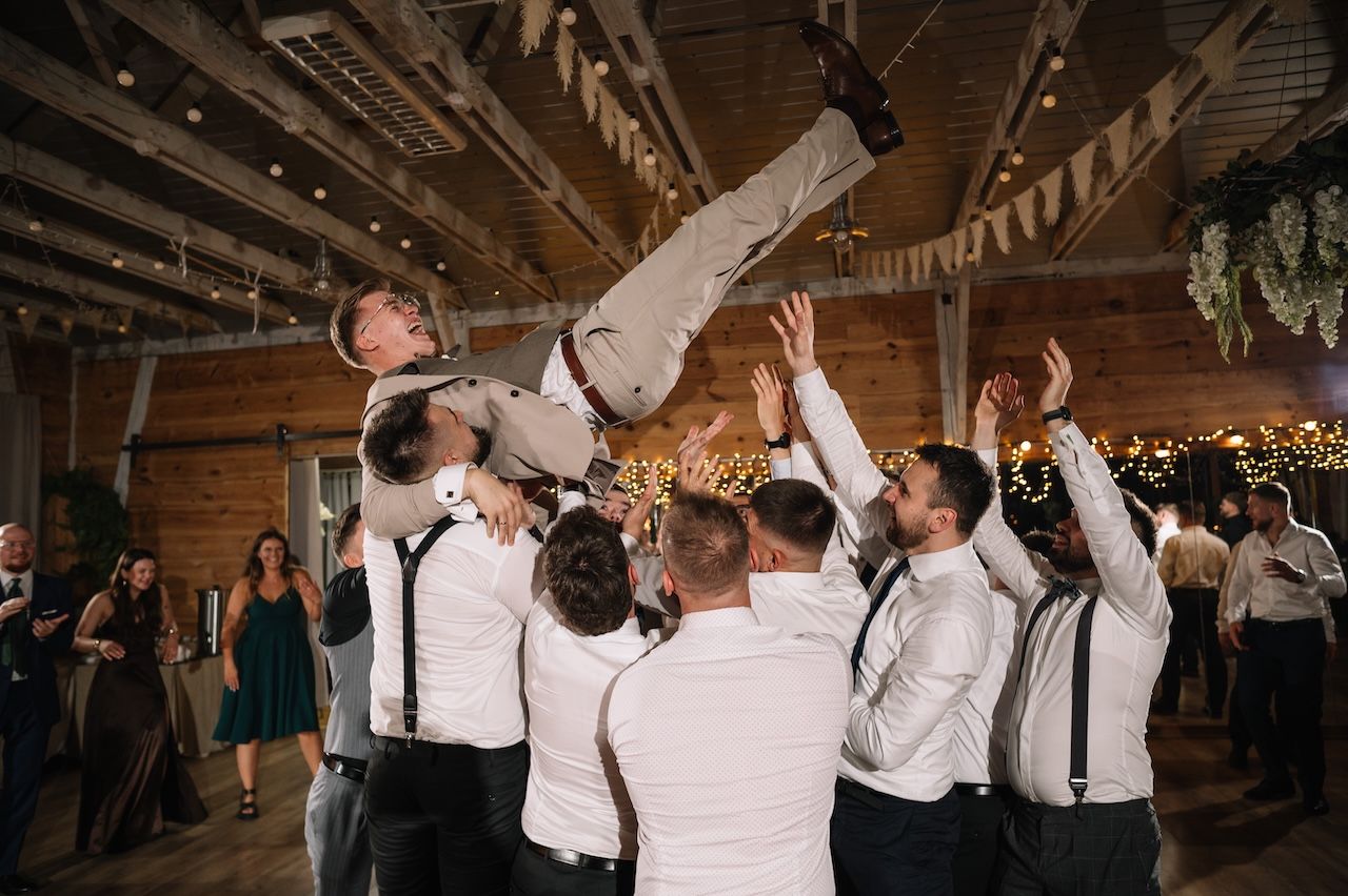 Groomsmen tossing the groom into the air during a lively wedding reception celebration.