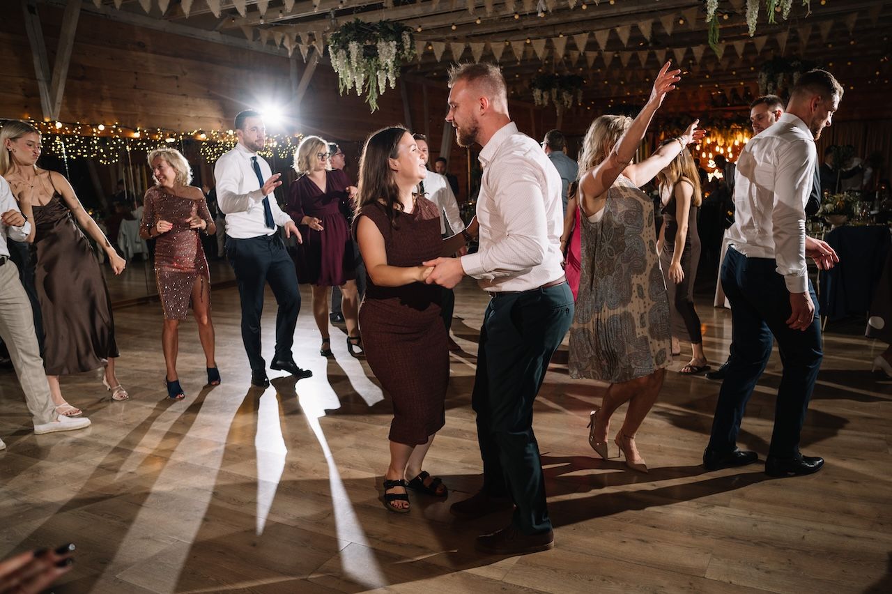 Couples dancing together on the dance floor at a warmly lit rustic wedding reception.
