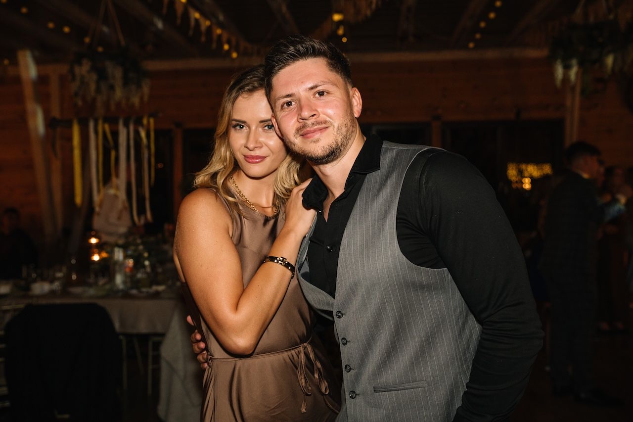 Elegant couple posing together at a dimly lit rustic wedding reception venue.