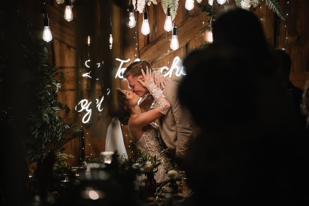 Bride and groom sharing a romantic kiss at a candlelit wedding reception table.