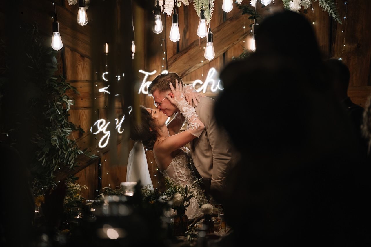 Bride and groom sharing a romantic kiss at a candlelit wedding reception table.