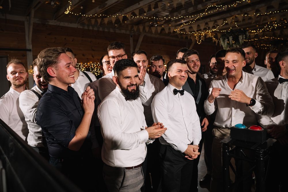 Group of men in white shirts laughing and clapping together at a wedding reception.