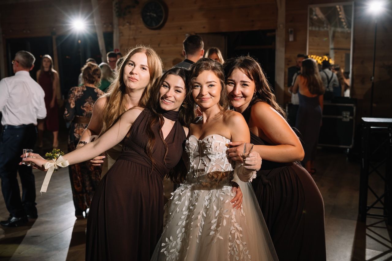 Bride in lace gown posing with three bridesmaids in brown dresses at wedding reception.