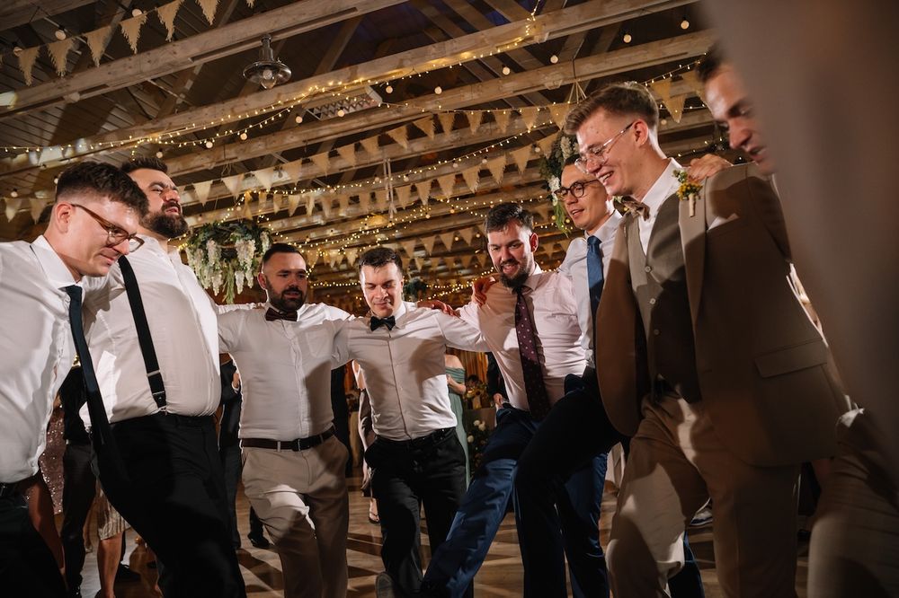 Groomsmen in white shirts and suspenders dancing together at a lively wedding reception.