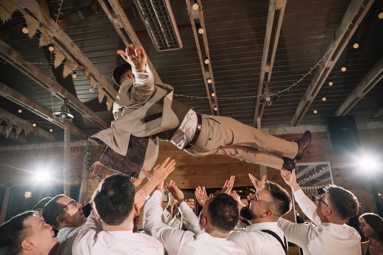 Groomsmen lifting and tossing the groom into the air at a wedding reception celebration.